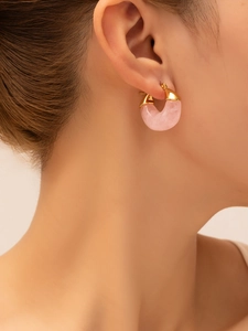 Detail shot of a pink resin C-shaped earring on model's ear with gold plating