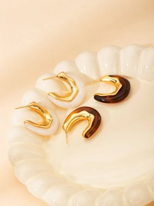 Detail of C-shaped resin earrings with marble and tortoiseshell patterns in gold metal