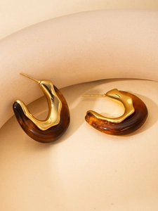 Detailed macro view of C-shaped titanium earrings featuring gold metal and tortoise resin