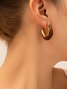 Close-up of elegant gold metal and amber resin C-shaped chunky earrings worn on model