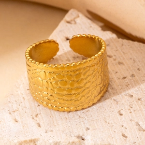 Detail shot of golden wide band ring with pebbled texture on beige stone