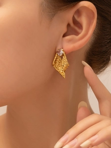 Macro shot of gold vintage titanium earring with square zircon and textured lava metal design