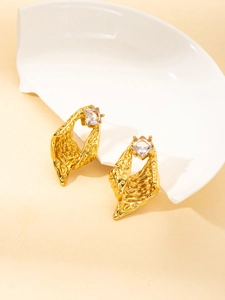 Detailed close-up of golden geometric earrings with textured lava pattern and zircon stone