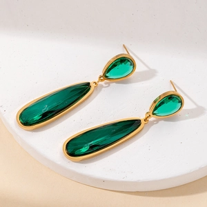 Detalle de pendientes de gota dorados con cristales verde esmeralda sobre piedra blanca