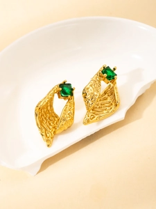 Detailed close-up of gold vintage earrings with irregular texture and green square gemstones