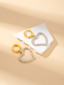 Detail of gold heart earrings with white crystals on a white stone pedestal