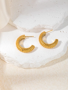 Close-up of golden C-shaped hoop earrings with beaded texture on a stone pedestal