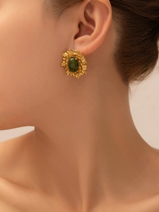 Close-up of gold titanium earring with oval green gemstone and vintage leaf texture