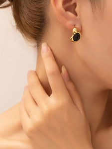 Close-up of a gold-plated vintage stud earring with a black oval gemstone on a model