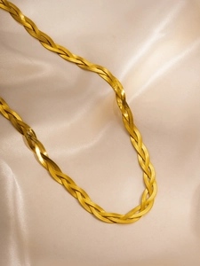 Macro detail of braided gold herringbone chain necklace on champagne silk satin background