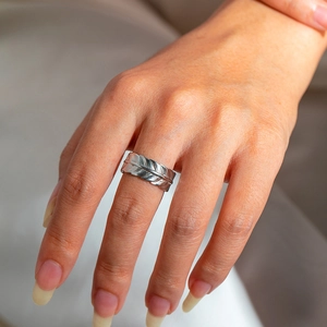 Close-up of adjustable silver feather ring with detailed texture on a soft fabric backdrop