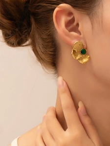 Macro detail of a vintage gold ginkgo leaf earring featuring a round green gemstone