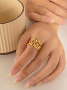 Dettaglio di un anello geometrico traforato dorato sulla mano con sfondo di tazza beige