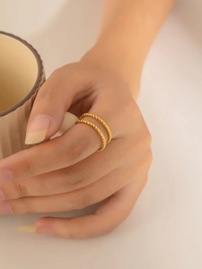 Dettaglio di un anello dorato a doppio strato con texture indossato da una modella