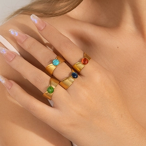 Detalle de anillos dorados multicapa con piedras turquesas de colores en los dedos del modelo