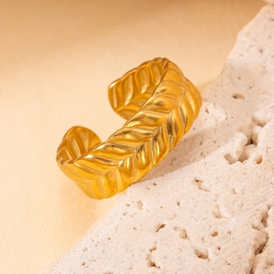 Détail macro d'une bague ouverte dorée avec motif chevron sur un support en pierre
