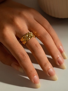 Détail d'une bague dorée en titane avec texture pyramidale et design large moderne