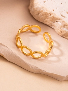 Detalle de anillo de acero al titanio dorado con eslabones ovales en superficie de piedra