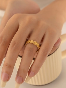 Detailaufnahme eines goldenen Gänseblümchen-Rings an der Hand vor einer Keramiktasse