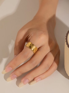 Vista detallada de un anillo ancho dorado con patrón de rombos en una mano real