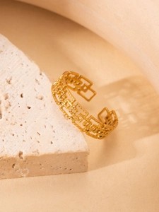 Detail of gold-plated open ring with hollow rectangular patterns on stone texture