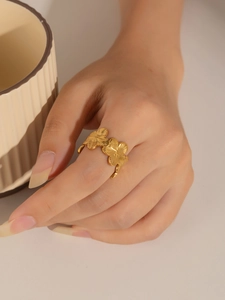Detalle de un anillo abierto floral dorado con pétalos cepillados en el dedo de una mujer