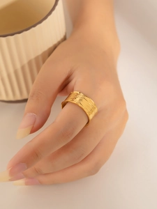 Close-up of wide gold-plated steel ring with unique hammered texture and brushed finish