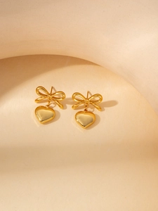 Detailed close-up of golden bowknot earrings with heart pendants on beige display
