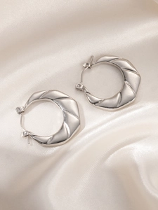 Detailed close-up of silver steel hoop earring with diagonal textured groove pattern
