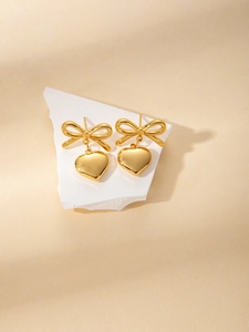 Close-up of golden bow and heart pendant earrings on a white stone display stand