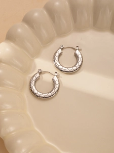 Macro shot of silver titanium steel hoop earrings with textured geometric patterns