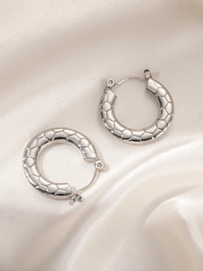 Close-up of silver hoop earrings featuring a textured snake scale geometric pattern