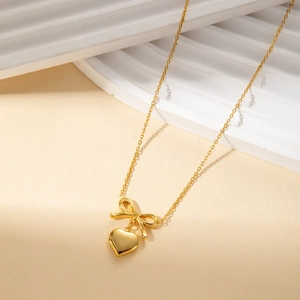 Golden bow and heart pendant necklace in titanium steel on minimalist display base