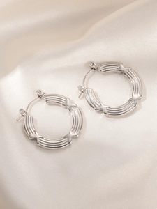 Detail view of silver hoop earrings with horizontal grooves and X-shaped cross decorations