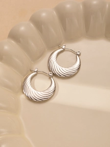 Detail of silver croissant hoop earrings with spiral texture on a beige ceramic tray
