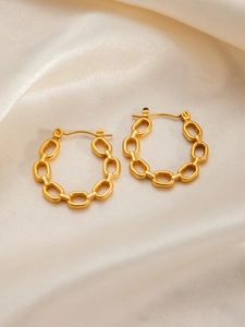 Detail of gold-plated chain link hoop earrings on a soft cream satin background