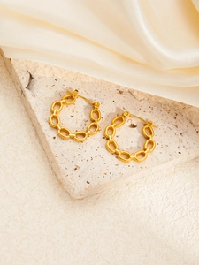 Close-up of gold titanium steel earrings with a retro hollow chain-link design on silk