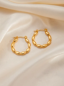 Macro detail of gold beaded olive link hoop earrings on white silk fabric background