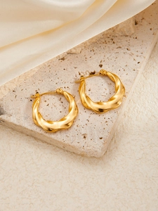 Detail of gold twisted hoop earrings with silk-matte finish on stone and silk background