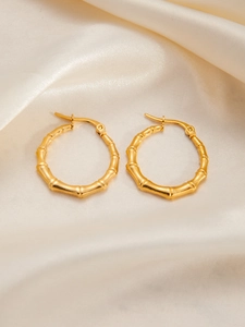 Detailed close-up of gold bamboo textured titanium steel hoop earrings on silk background