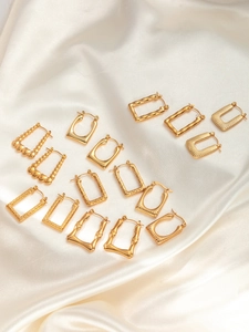 Details von goldenen geometrischen Edelstahl-Ohrringen auf weißem Seidenstoff