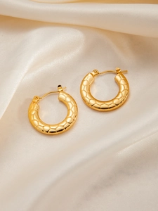 Macro view of gold hoop earrings with textured hexagonal honeycomb pattern on silk