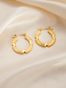 Detailed macro view of triple-layered gold-plated hoop earrings on champagne silk background