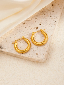 Detail of gold-plated hoop earrings with textured diamond pattern on stone surface