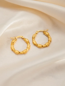 Macro shot of gold-plated titanium earrings with elegant twisted texture on silk cloth
