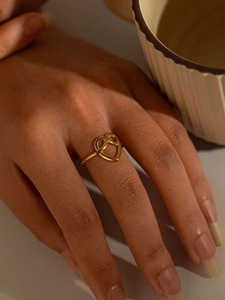 Macro shot of gold intertwined heart knot ring showing polished mirror surface on finger