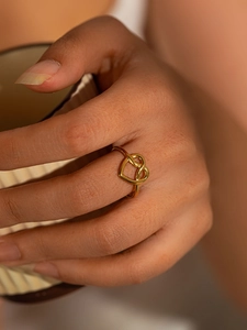 Close-up of golden titanium steel heart knot ring worn while holding a ceramic cup