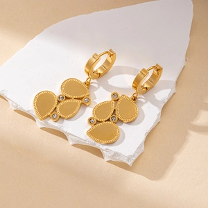 Detailed macro view of gold drop earrings with white zircons on a white stone display