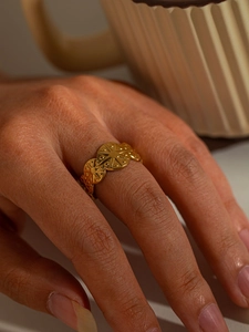 Detail of gold titanium steel ring with sunburst embossed design worn on finger