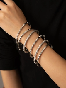 Detail of six silver-toned minimalist bangles featuring bamboo and twisted metal textures
